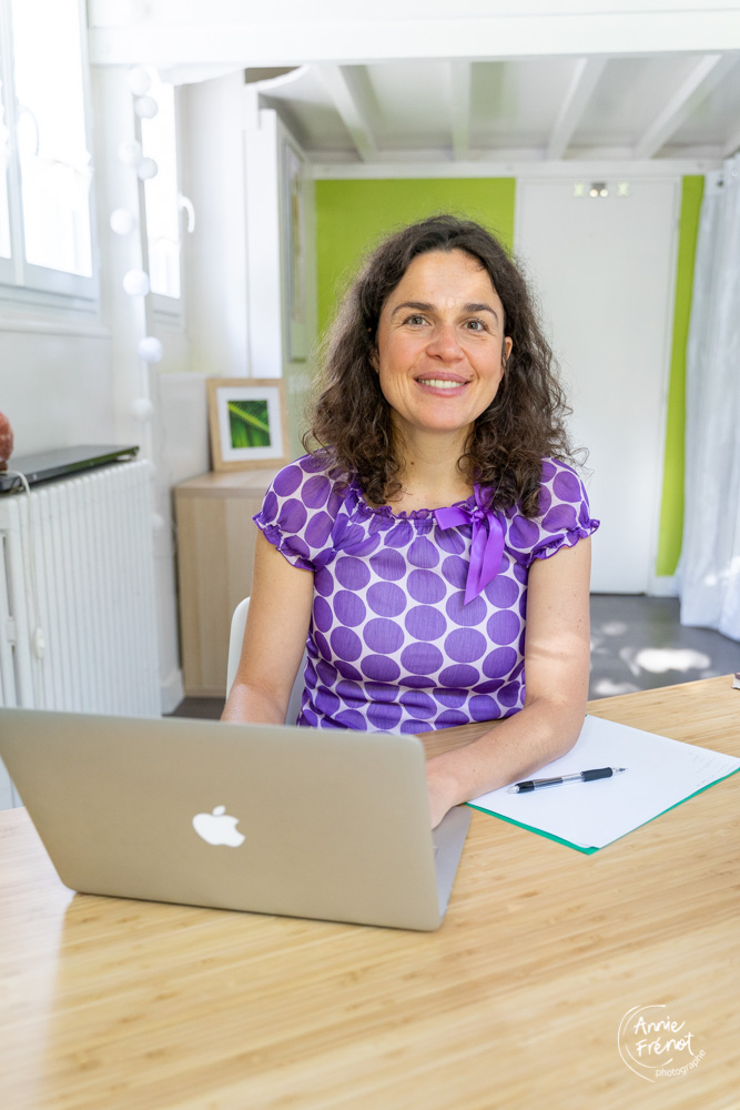 Isabelle Schillig naturopathe est assise à son bureau avec un ordinateur et regarde l'objectif à l'écoute.